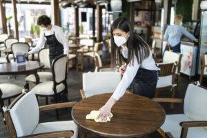 The girl is wiping the table in the restaurant.