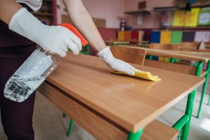 A woman wiping a table, showcasing school cleaning services in action.