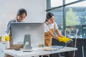 Two professional cleaners are wiping down tables in office spaces to deal with seasonal pollen.