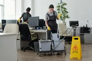 Two professional cleaners are performing a deep cleaning in the office, which is essential for employee productivity during working hours.
