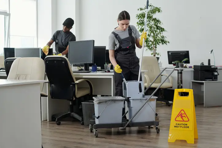 Two professional cleaners are performing a deep cleaning in the office, which is essential for employee productivity during working hours.