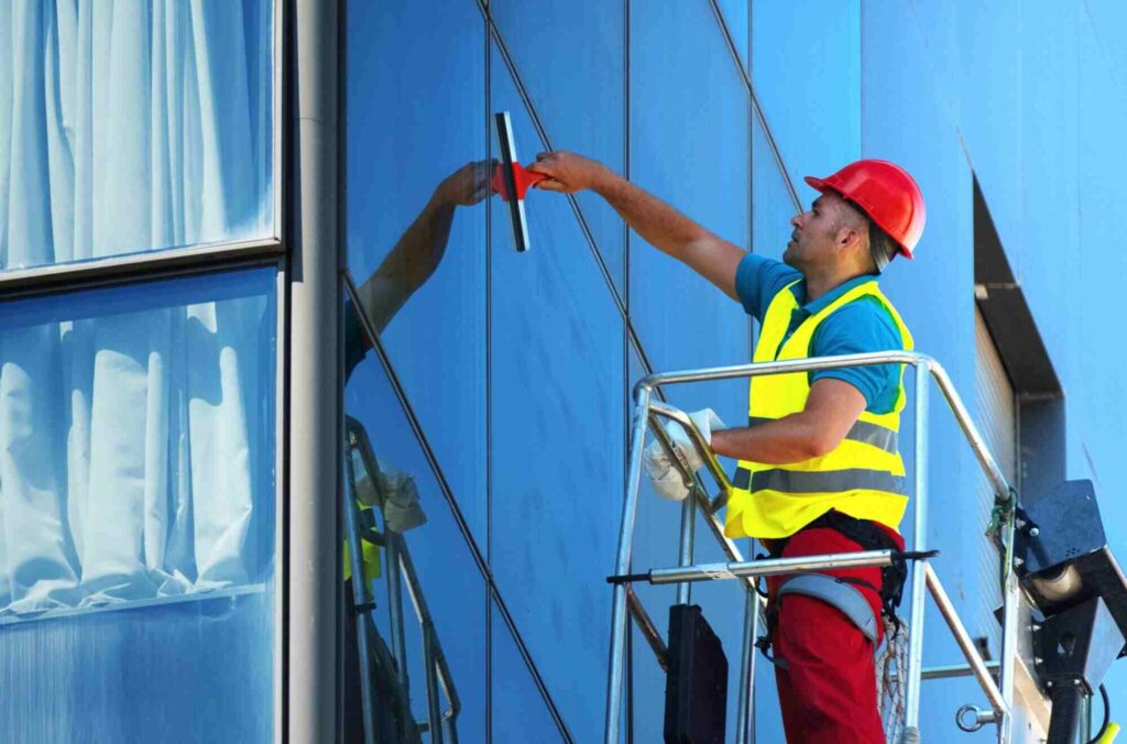 Technician cleaning exterior commercial windows on a building lift showing how much commercial window cleaning cost depends on height, access, and labour requirements.