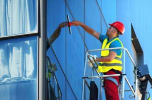 Technician cleaning exterior commercial windows on a building lift showing how much commercial window cleaning cost depends on height, access, and labour requirements.