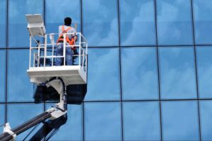 Worker using lift equipment to clean high-rise glass building illustrating how to price commercial window cleaning based on building height and access complexity.