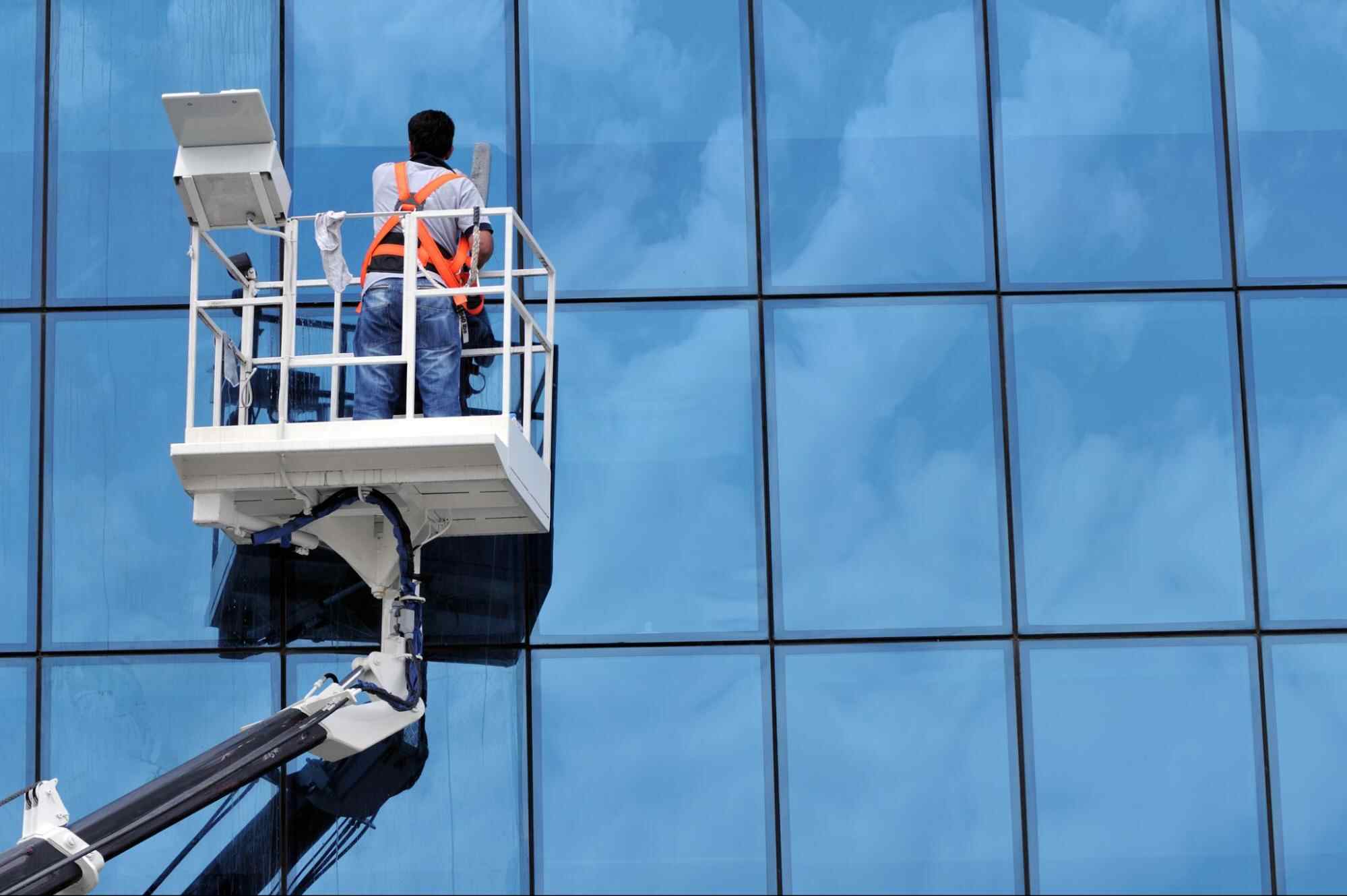Worker using lift equipment to clean high-rise glass building illustrating how to price commercial window cleaning based on building height and access complexity.